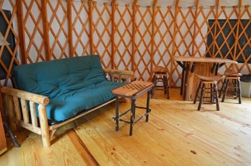 Cozy interior of a yurt featuring a sofa, wooden table, and stools on a wooden floor.