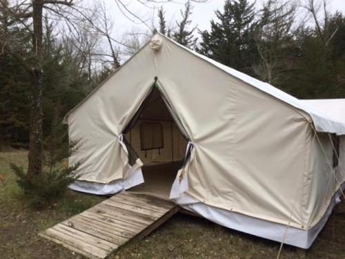 A large beige canvas tent with an open entrance, set in a wooded area with trees in the background.