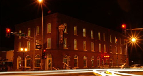 Historic brick hotel at night, illuminated by streetlights and traffic signals, with a café sign visible.