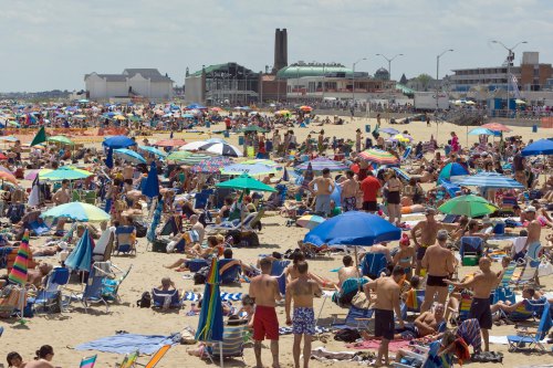 A crowded beach scene with numerous umbrellas, sunbathers, and people enjoying the sunny day by the water.