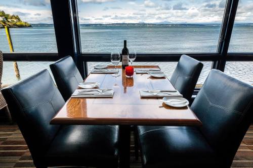 A dining table set for four, overlooking a scenic waterfront view with a bottle of wine and a candle.