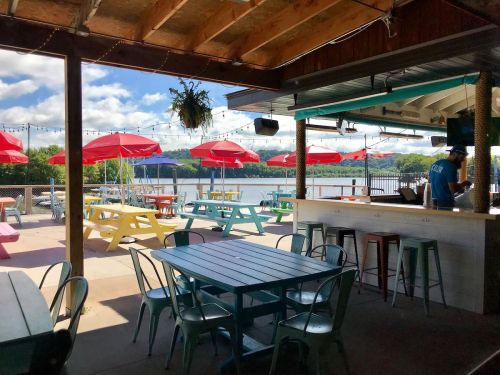Outdoor dining area with colorful picnic tables, red umbrellas, and a view of the water under a blue sky.