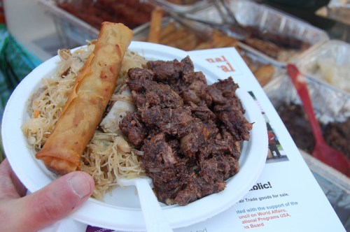 A plate of food featuring seasoned beef, fried rice, a spring roll, and a flyer in the background.