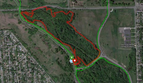 Map showing a wooded area with marked trails in red, surrounded by roads and nearby educational facilities.