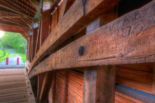Close-up of wooden beams inside a covered bridge, featuring carved initials and dates on the weathered wood.