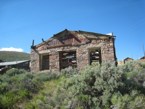 Abandoned stone building surrounded by green shrubs under a clear blue sky.