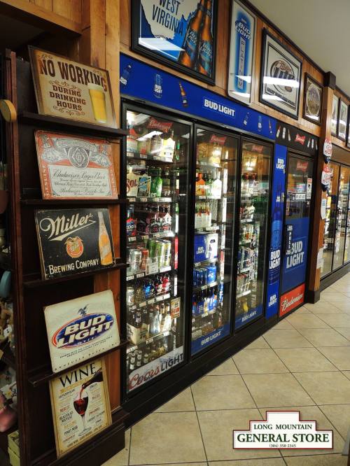 A general store aisle featuring beverage coolers with various beer brands and signs about store policies.