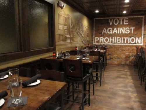 Interior of a restaurant with wooden tables, chairs, and a mural featuring "Vote Against Prohibition" on the wall.