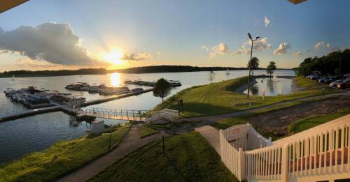 A serene lakeside view at sunset, featuring boats docked and lush green grass along the water's edge.