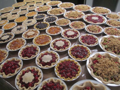 A large display of various fruit pies arranged on a table, showcasing different fillings and crust designs.