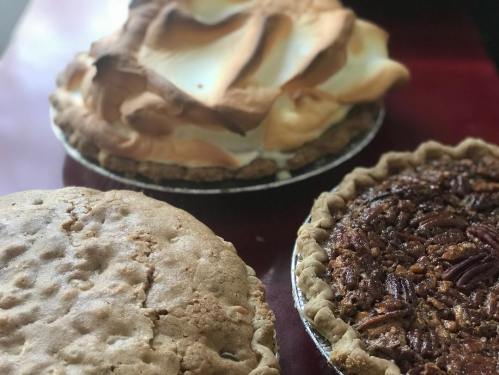 Three pies on a table: a meringue pie, a pecan pie, and a cookie pie, showcasing various textures and colors.