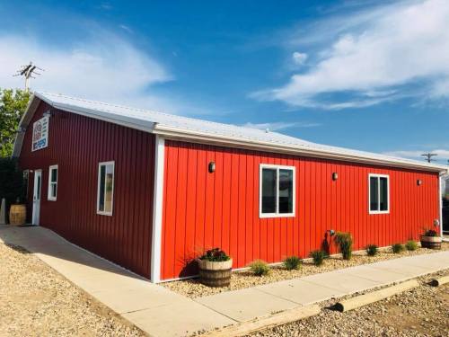 A bright red building with a metal roof, featuring windows and a walkway, set against a clear blue sky.