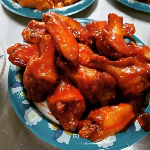 A plate of saucy chicken wings piled high, served on a decorative paper plate.