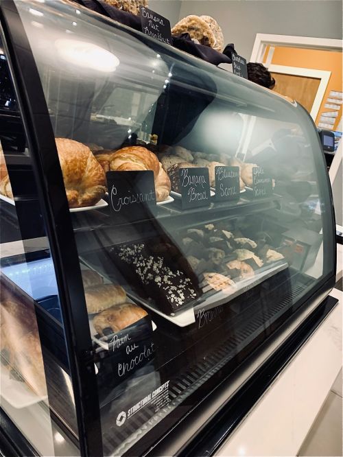 A display case filled with various baked goods, including croissants, banana bread, and pastries.