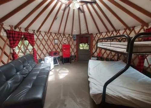 Interior of a yurt featuring a black sofa, bunk beds, and rustic decor with plaid curtains.