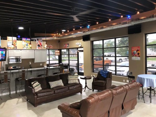 A modern lounge area with brown sofas, a kitchen, and large windows, featuring a casual, inviting atmosphere.