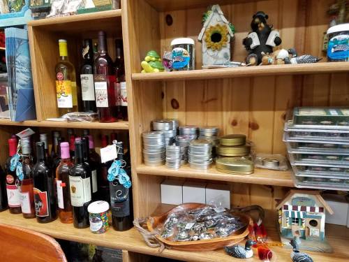 A wooden shelf displaying various bottles of wine, decorative items, and small tins, creating a cozy shop atmosphere.