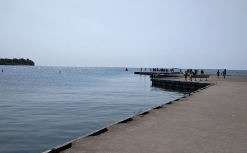 A calm waterfront scene with a concrete pier extending into the water and people enjoying the area under a clear sky.