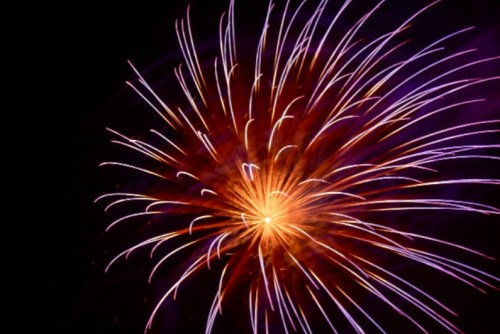 A vibrant firework explosion with bright orange and purple trails against a dark night sky.