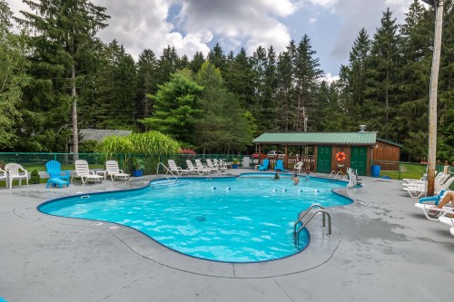 A swimming pool surrounded by lounge chairs, with trees in the background and a small building nearby.