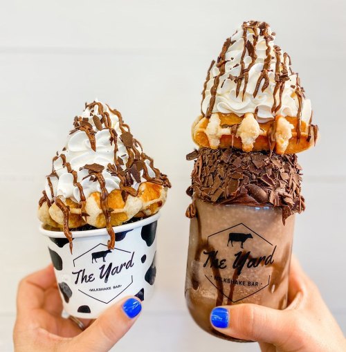 Two decadent desserts: a cup of soft serve topped with chocolate drizzle and a towering milkshake with whipped cream and toppings.