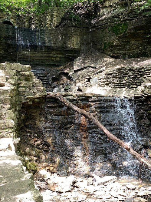 A rocky landscape with a small waterfall cascading down, surrounded by greenery and stone formations.