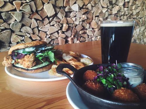 A plate with a fried chicken sandwich, chips, and a small skillet of croquettes, alongside a glass of dark beer.