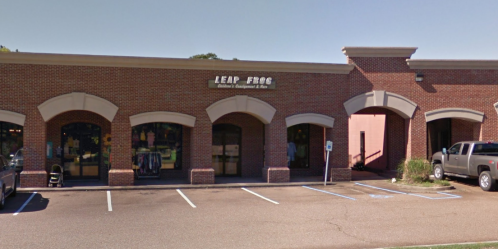 Exterior of a brick building with "Leap Frog" sign, featuring storefronts and parking spaces in front.
