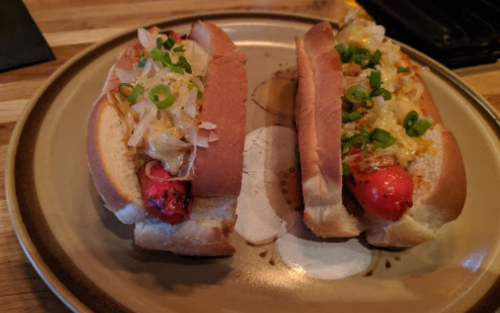 Two hot dogs on a plate: one topped with sauerkraut and the other with cheese and green onions.