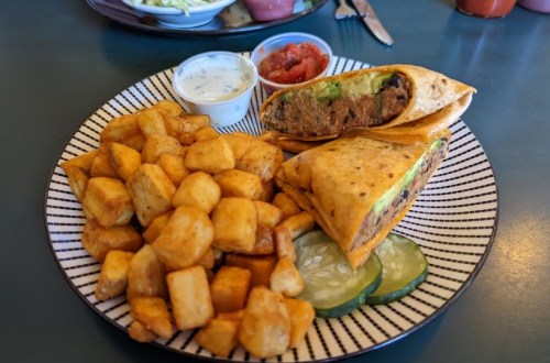A plate with two wrapped burritos, crispy potatoes, pickles, and dipping sauces.