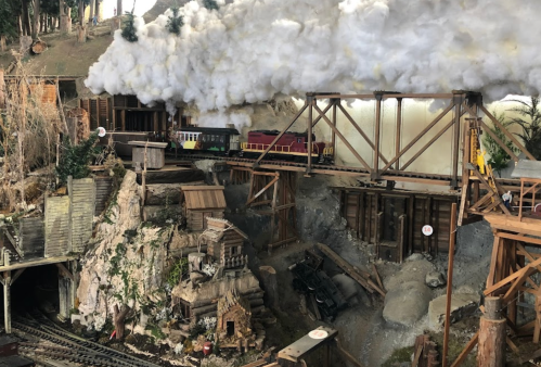 A miniature train scene with smoke, featuring a bridge over a rocky landscape and detailed structures.