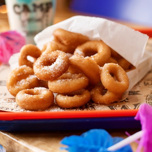 A colorful plate of mini donuts dusted with powdered sugar, served in a paper container with festive decorations.