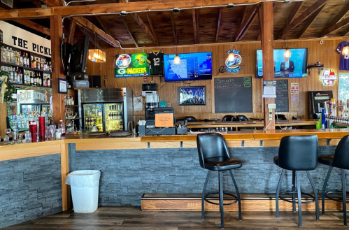 Interior of a bar with a wooden ceiling, multiple TVs, a well-stocked bar, and high stools.