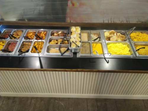 A buffet with various food items including meats, breads, and scrambled eggs in metal trays.