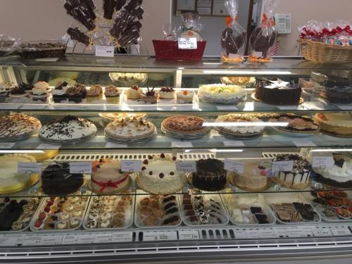 A display case filled with various cakes and desserts, including chocolate cakes, cheesecakes, and pastries.