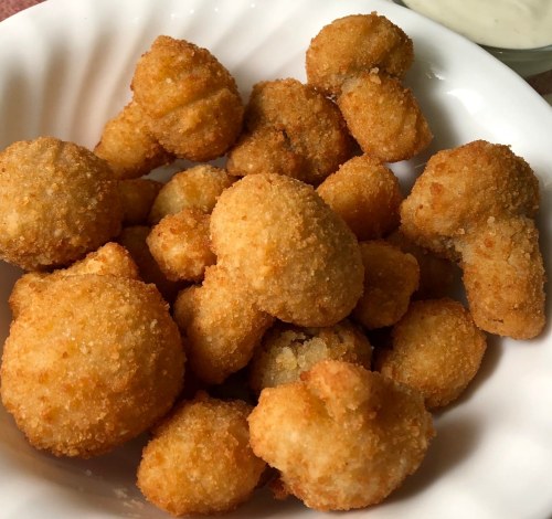 A bowl of golden-brown, crispy fried snacks, resembling small balls and shapes, served with a side of dipping sauce.