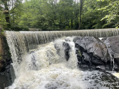 A serene waterfall cascades over rocky ledges, surrounded by lush green trees and a peaceful natural setting.