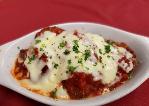 A dish of breaded chicken topped with marinara sauce and melted cheese, garnished with parsley, served in a white dish.