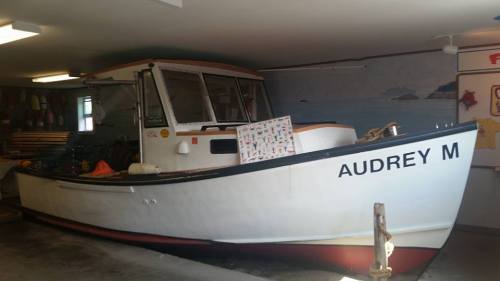 A white boat named "AUDREY M" is parked inside a garage, with colorful surfboards and a mural in the background.