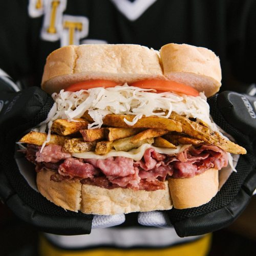 A large sandwich with layers of meat, fries, sauerkraut, and tomato, held between two slices of bread.
