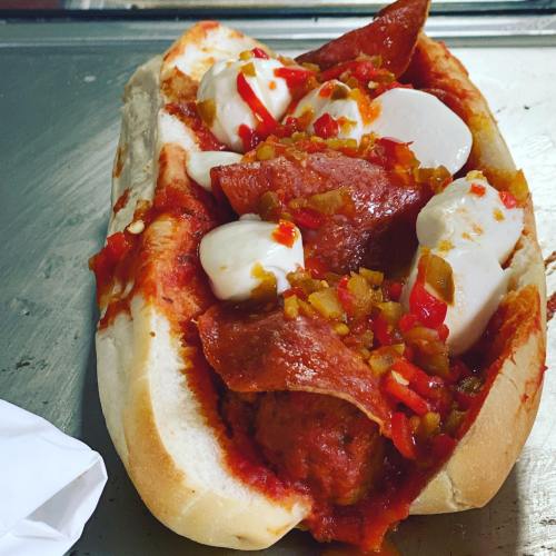 A loaded sandwich with meatballs, pepperoni, mozzarella, and diced peppers in a soft bun, topped with marinara sauce.