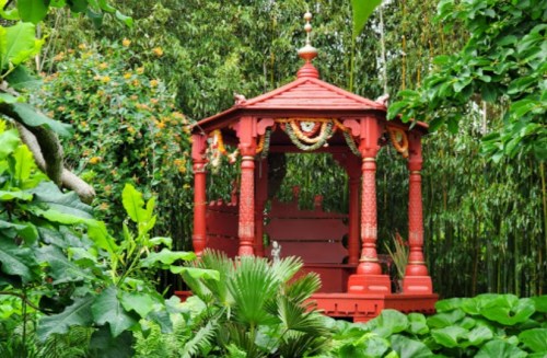A vibrant red gazebo surrounded by lush green foliage and tropical plants.