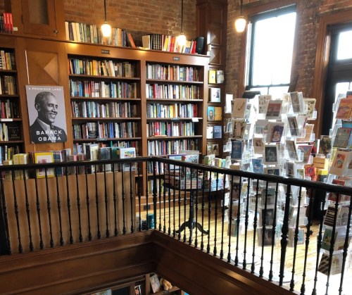 A cozy bookstore with shelves of books, a poster of Barack Obama, and a display of greeting cards.