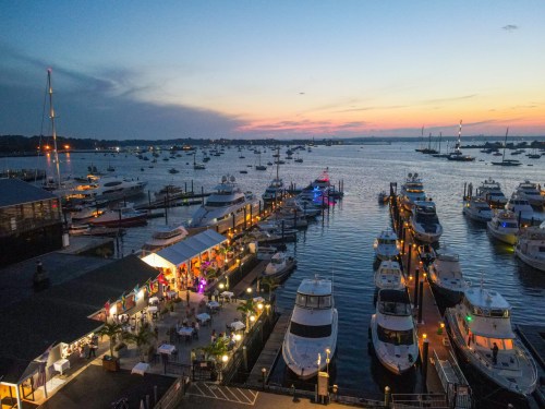 A scenic marina at sunset, featuring boats docked and a lively waterfront restaurant with colorful lights.