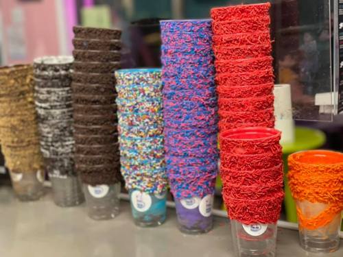 A row of colorful cups with various toppings, including sprinkles and chocolate, stacked on a counter.