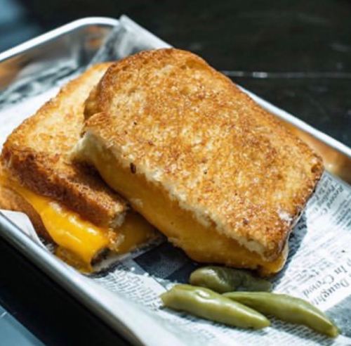 A golden-brown grilled cheese sandwich on a tray, accompanied by pickled green peppers.