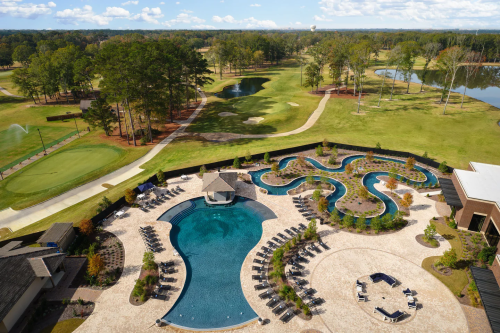 Aerial view of a resort pool area with winding pools, lounge chairs, and a golf course in the background.
