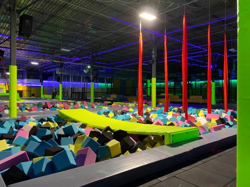 A colorful indoor trampoline park featuring a foam pit filled with multicolored blocks and hanging aerial silks.
