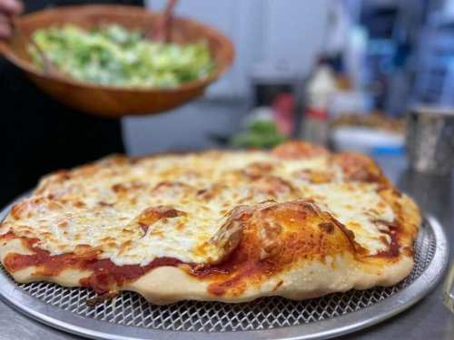 A freshly baked cheese pizza on a cooling rack, with a bowl of salad in the background.