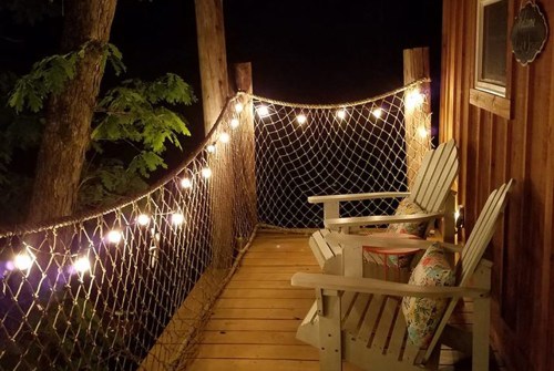 A cozy porch at night with string lights, wooden chairs, and a view of trees.